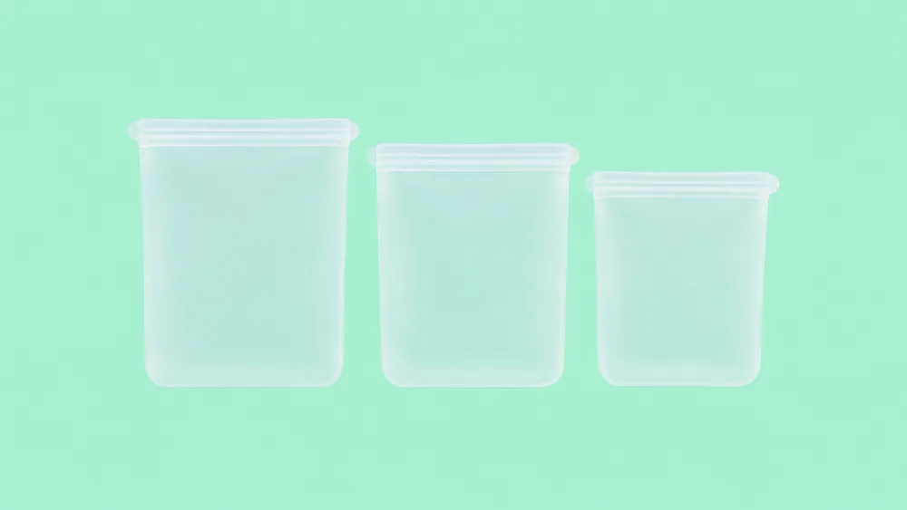 Three reusable silicone food storage bags in a row on a mint green background